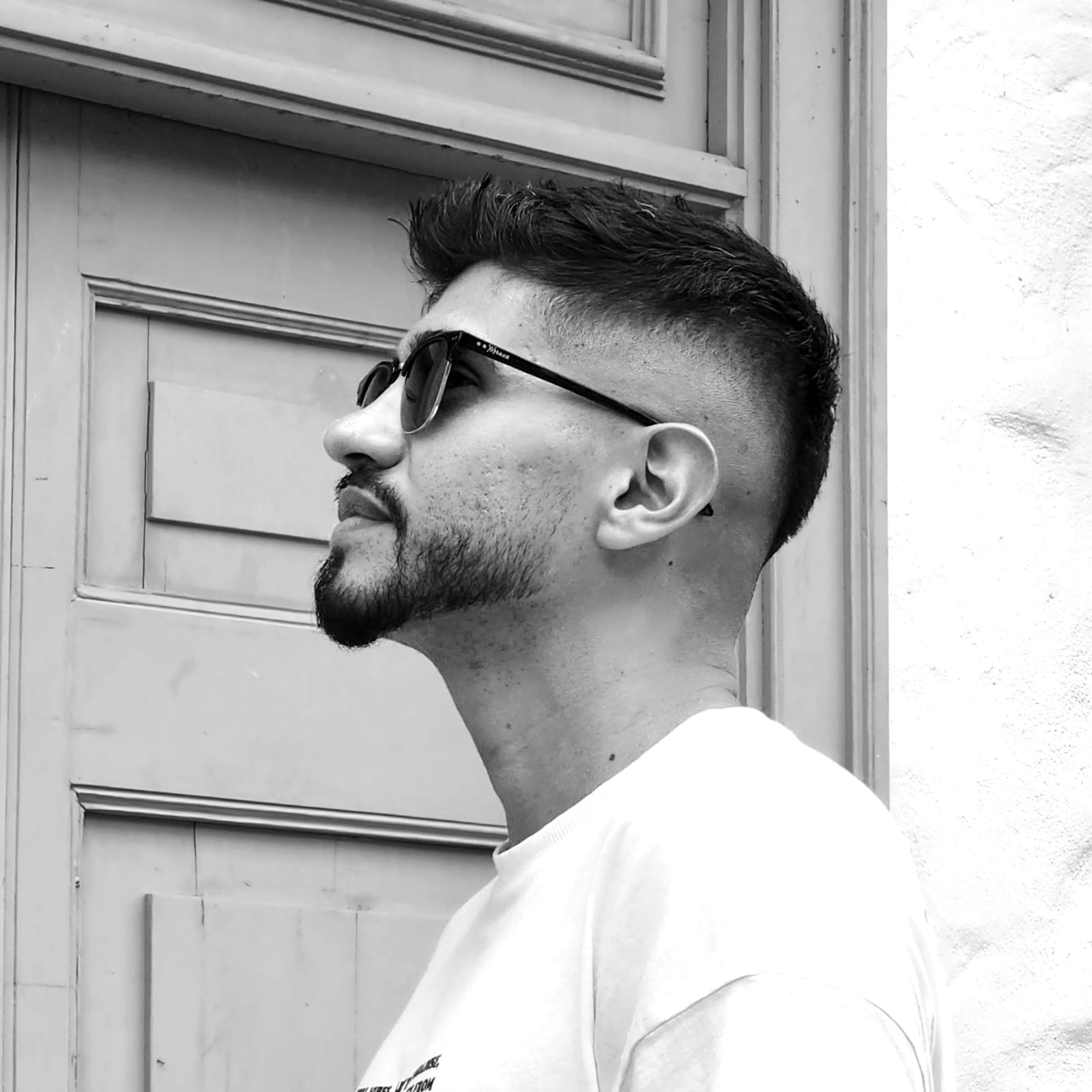 Black-and-white portrait of Andrés Solórzano in profile, wearing sunglasses in front of a paneled door.