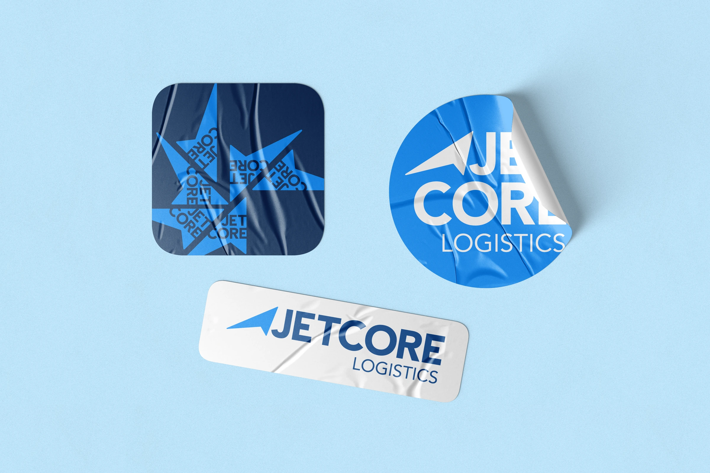 Conceptual application mockup: three Jetcore stickers on a pale blue surface, with rectangular, square and circular configurations, blue patterns and the directional symbol.