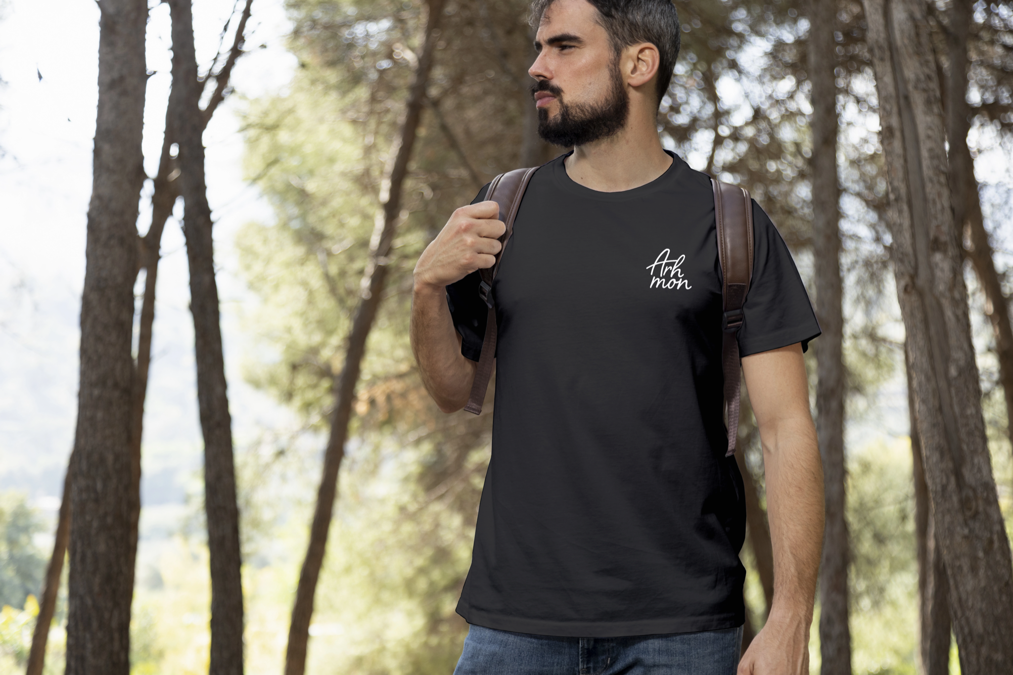 Intended application mockup: a person outdoors wearing a black t-shirt with the small white Arhmon handwritten mark on the chest.