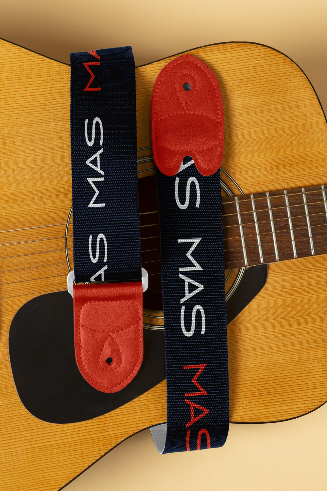 Brand application mockup: two navy guitar straps with the repeated MAS wordmark and red leather ends, laid over an acoustic guitar.